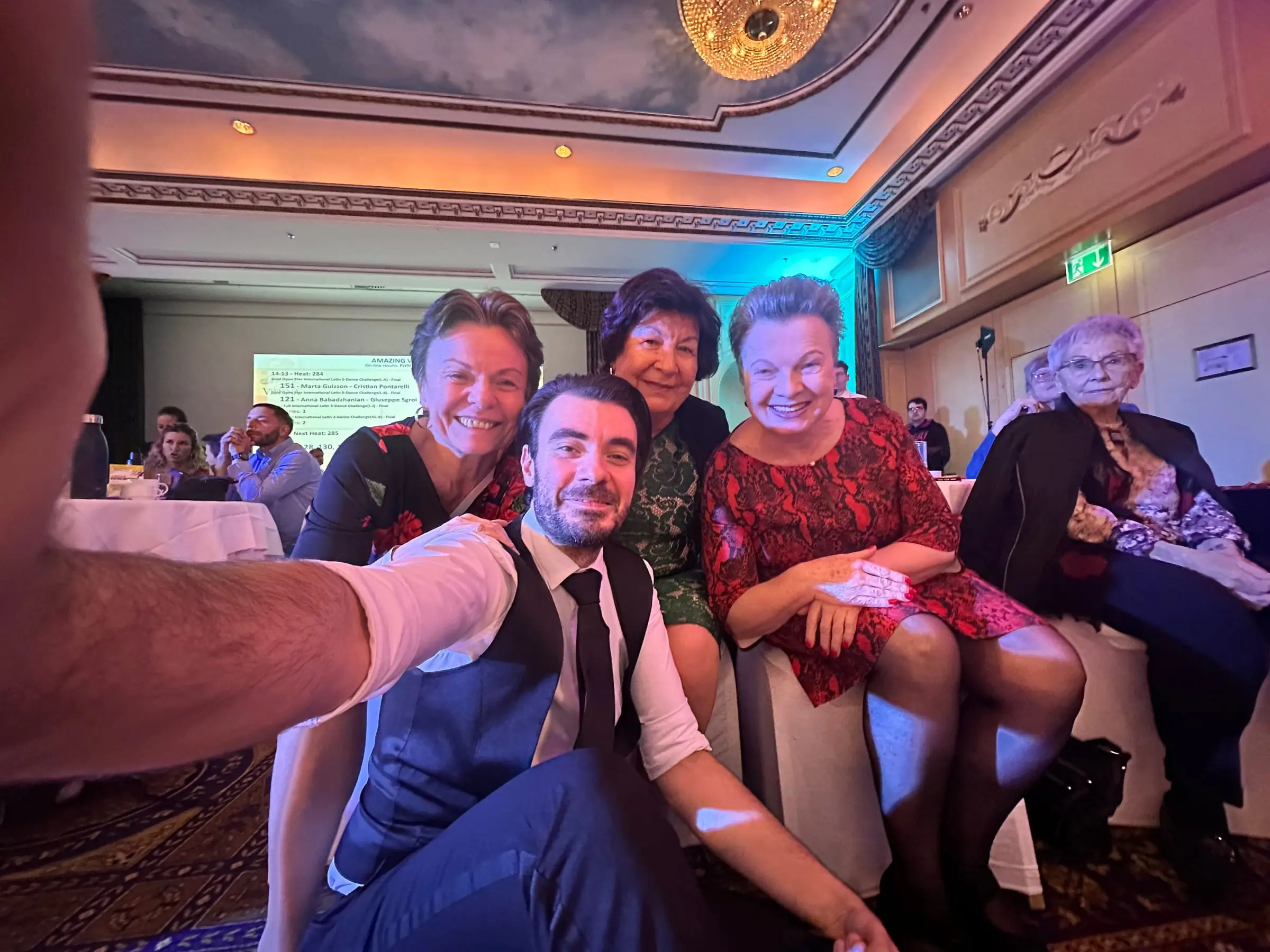 Selfie von fünf Personen an einem Tisch im Ballsaal, im Hintergrund eine Leinwand